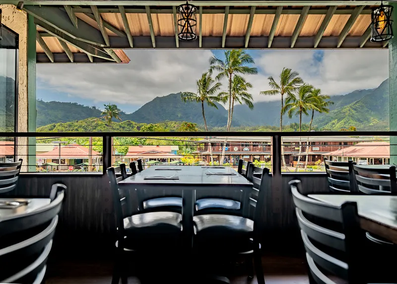 Table on the open-air terrace with palm trees and Hanalei's green mountains